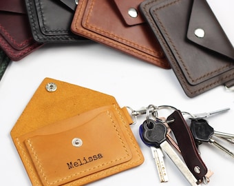 May include: Leather keychains in various colors, including brown, black, and tan. One keychain is open, revealing a card holder with the name "Melissa" printed on it. A set of keys is attached to the open keychain.