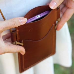 Puede incluir: Una funda de tel&eacute;fono de cuero marr&oacute;n con una correa. La funda tiene una solapa que se cierra con un broche. Un tel&eacute;fono morado est&aacute; dentro de la funda.