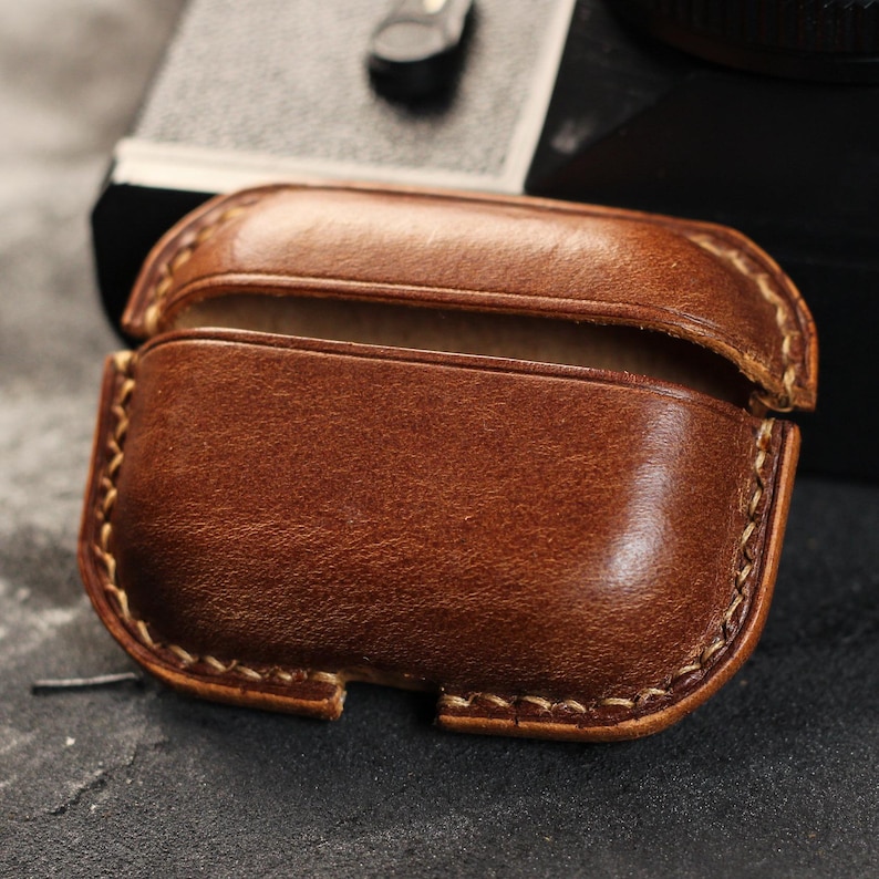 May include: A brown leather case with a stitched edge for AirPods or other small electronics.