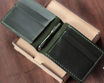 May include: A dark green leather wallet with a money clip and multiple card slots. The wallet is open and lying on a wooden surface.