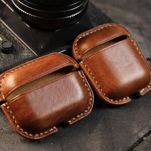 May include: Two brown leather cases for wireless earbuds. The cases have a stitched edge and are made of a soft, supple leather.