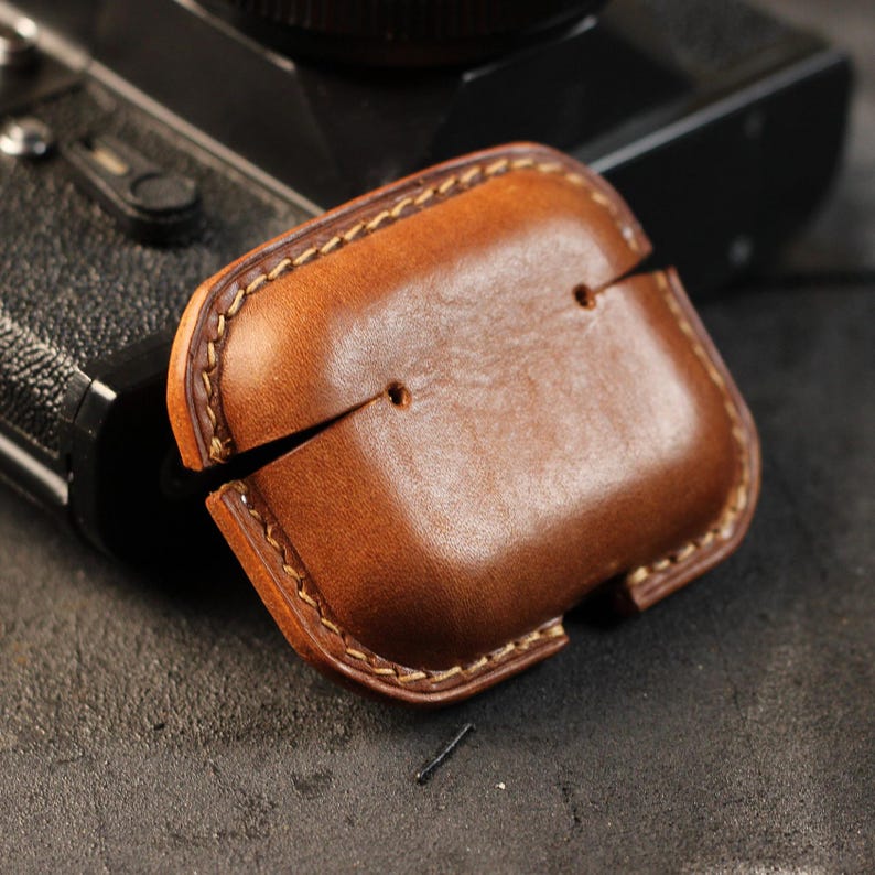 May include: A brown leather case with stitching around the edges. The case has a flap that opens to reveal a space for a small electronic device.