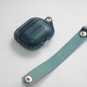 May include: A blue leather case for wireless earbuds with the text "Soul Therapy" embossed on the front. The case is attached to a blue leather strap.