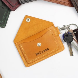 May include: Open, tan leather key holder with a snap closure and the name "Melissa" stamped on the front. A silver keyring is attached, holding several keys. Other leather key holders in various colors are visible.