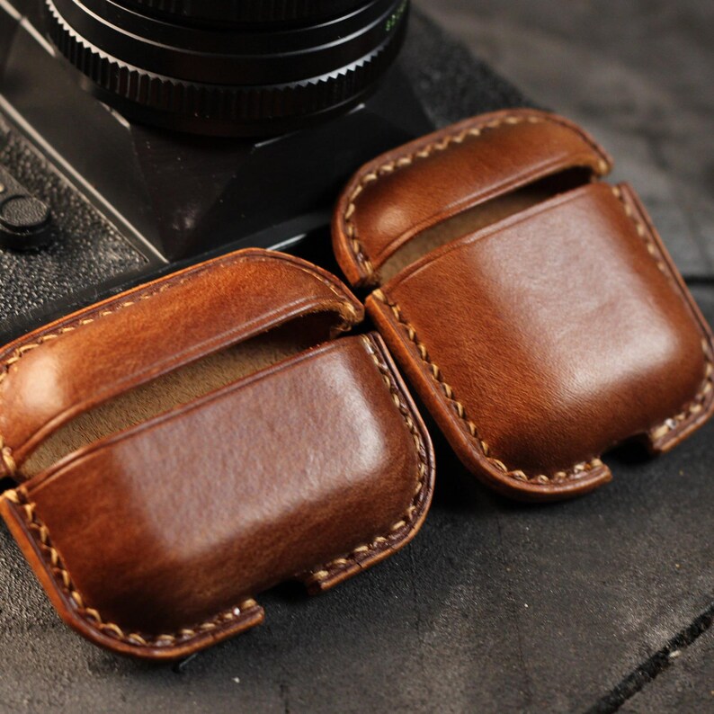 May include: Two brown leather cases for wireless earbuds. The cases have a stitched edge and are made of a soft, supple leather.