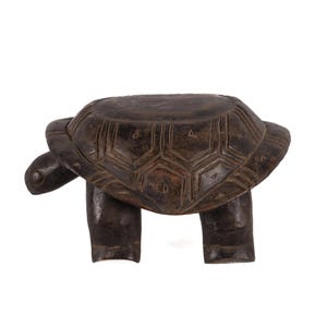 May include: A dark brown, carved wooden turtle-shaped stool. The stool features a detailed turtle shell design on the top and four sturdy legs. The turtle's head and tail extend from the shell. The stool is a unique piece of home decor.