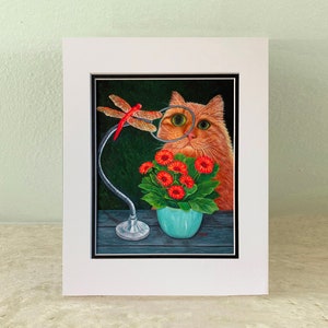 Puede incluir: Pintura enmarcada de un gato naranja mirando una libélula a través de una lupa. Debajo hay una maceta turquesa con flores rojas. La obra de arte está sobre un fondo verde oscuro.