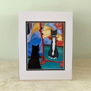 Könnte beinhalten: Eine schwarz-weiße Katze betrachtet ihr Spiegelbild in einem bunten Spiegel. Die Katze sitzt auf einer roten Plattform. Der Spiegel ist von einem bunten, abstrakten Design umgeben.