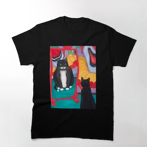 Könnte beinhalten: Eine schwarz-weiße Katze mit einer weißen Brust schaut in einen roten und blauen Spiegel. Eine schwarze Katze steht hinter dem Spiegel und schaut die Katze im Spiegelbild an.