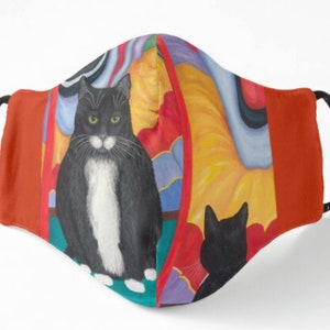 Könnte beinhalten: Eine Gesichtsmaske mit einem Gemälde einer schwarz-weißen Katze mit grünen Augen. Die Maske hat verstellbare schwarze Ohrschlaufen und einen lebendigen abstrakten Hintergrund mit roten, gelben und blauen Farbtönen.