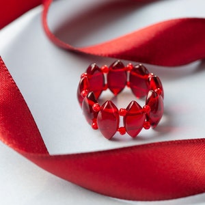 Op de afbeelding: Een rode kralenring met ovale kralen. De ring ligt op een rood satijnen lint.