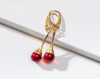 May include: A pair of gold cherry earrings with red glass stones.