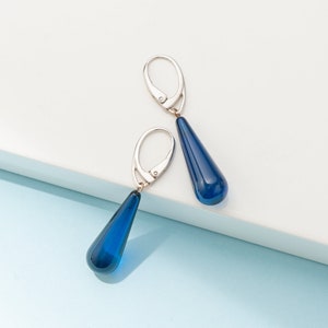 Op de afbeelding: Een paar zilveren druppelvormige oorbellen met blauwe glazen druppels.