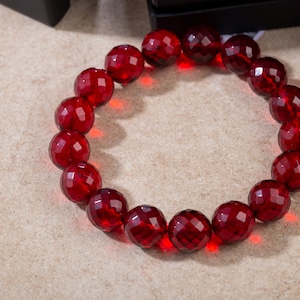 Op de afbeelding: Een rode edelsteen armband met gefacetteerde kralen. De armband is gemaakt van veel kleine, ronde kralen die allemaal dezelfde grootte hebben. De kralen zijn diep rood van kleur en hebben een glanzende afwerking.