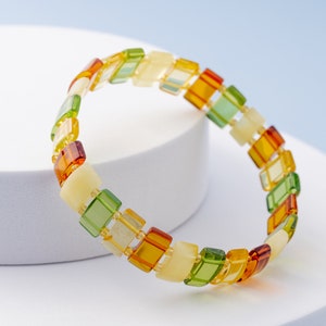Könnte beinhalten: Ein Armband aus Bernsteinperlen in Grün-, Gelb- und Orangetönen. Die Perlen sind rechteckig und in einem sich wiederholenden Muster angeordnet.