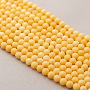 May include: A strand of round, pale yellow beads. The beads are consistent in size and colour, with a matte finish. The beads are strung together, forming a continuous line. Suitable for jewellery making.
