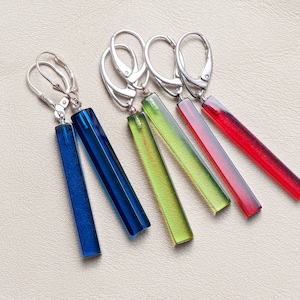 May include: A set of four pairs of dangle earrings with silver hooks. The earrings feature long, rectangular glass beads in shades of blue, green, and red.