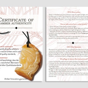 May include: A pendant made of amber, featuring a carved profile, hangs from a black cord. The pendant is a warm, golden color. The image includes a certificate of authenticity with text in English and German.