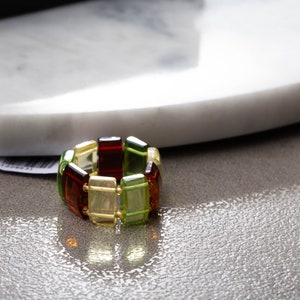 Könnte beinhalten: Ein mehrfarbiges Armband aus rechteckigen, bernsteinfarbenen Perlen. Das Armband besteht aus grünen, gelben und braunen Perlen.