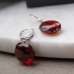 May include: A pair of silver earrings with red gemstone drops. The earrings have a simple design with a small hoop and a dangling gemstone.