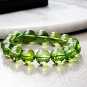 Puede incluir: Un brazalete de piedras preciosas verdes con cuentas redondas. El brazalete está hecho de piedras naturales y tiene un acabado pulido.