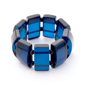 Könnte beinhalten: Ein blau-schwarzes Armband mit rechteckigen Gliedern. Das Armband besteht aus durchscheinendem blauem Material mit schwarzen Akzenten. Die Glieder sind durch kleine, dunkelblaue Perlen verbunden. Das Armband wird vor weißem Hintergrund gezeigt.