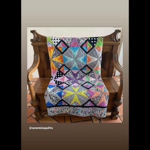 May include: A colorful quilt with geometric star and diamond patterns, draped over a wooden chair. The quilt features a variety of fabrics in shades of blue, yellow, pink, and gray, with black and white polka dot and floral accents. The text "tula pink" is visible.