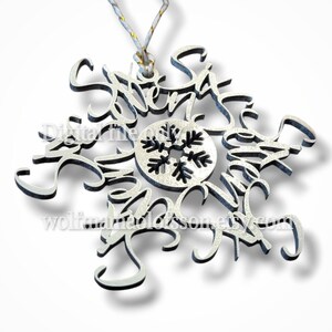 May include: A silver snowflake ornament with black trim and the word "Snow" in a cursive font. The ornament has a small snowflake design in the center and a gold and white string for hanging. The Etsy shop name is visible.