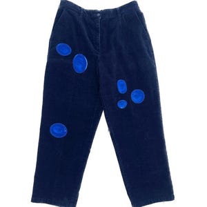 Puede incluir: Pantalón de pana azul oscuro con círculos de tela azul cosidos en la parte delantera.
