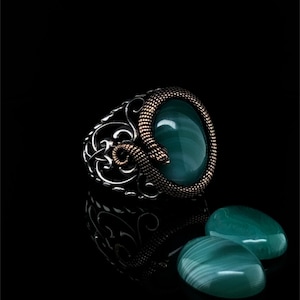 Puede incluir: Un anillo de plata con una piedra verde y un diseño de serpiente. El anillo está rodeado de dos piedras verdes.