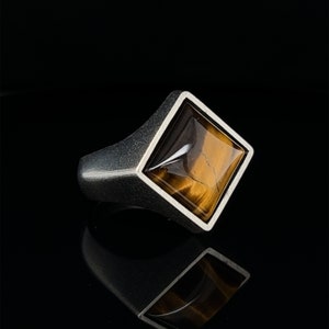 May include: A silver ring with a square-shaped tiger's eye gemstone.