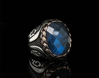 May include: A silver ring with a blue gemstone set in a gold-toned bezel. The ring has an intricate design with a braided band and a detailed setting.