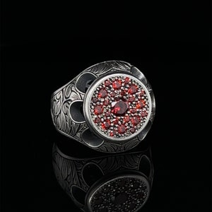 May include: A silver ring with an intricate design and a large red gemstone in the center.