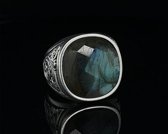 May include: A silver ring with an ornate design and a large, faceted, dark blue and green gemstone.