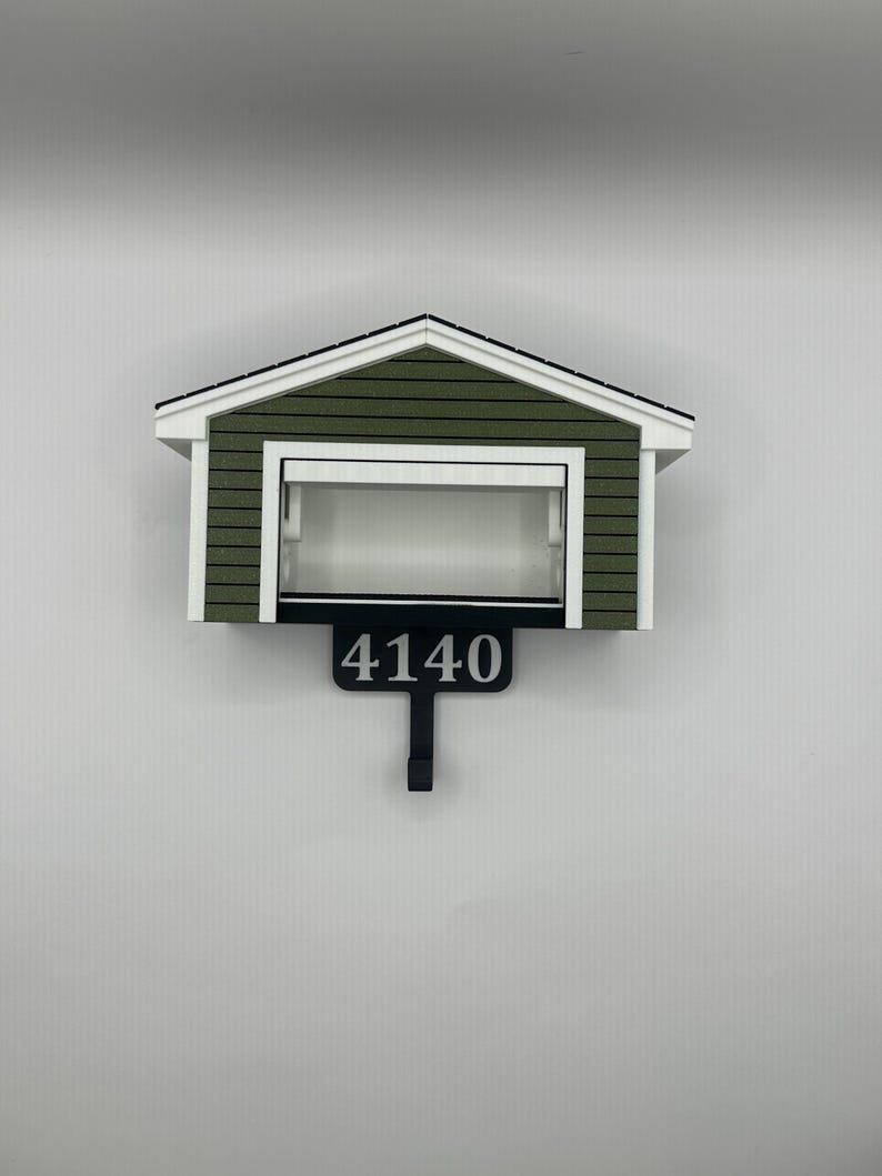 Op de afbeelding: Een huisvormige brievenbus met een groen en wit exterieur. De brievenbus heeft het nummer "4140" in zwart op een zwart bord met een haak eronder. Het dak is wit met zwarte rand.