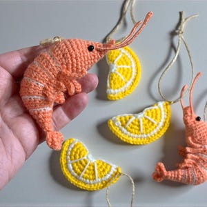 May include: Crocheted shrimp and lemon slice ornaments. The shrimp are orange with white stripes, and the lemon slices are yellow with white rinds. Each ornament has a string for hanging. Great for nautical or summer decor.