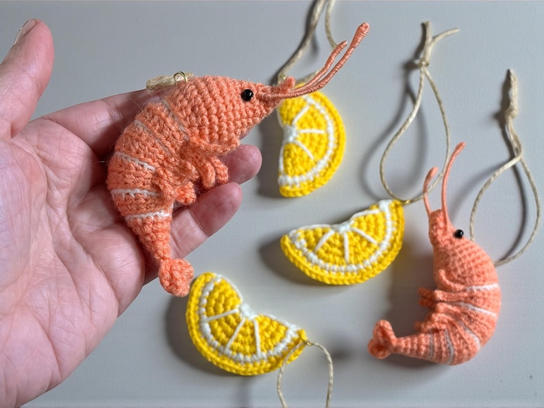 May include: Crocheted shrimp and lemon slice ornaments. The shrimp are orange with white stripes, and the lemon slices are yellow with white rinds. Each ornament has a string for hanging. Great for nautical or summer decor.