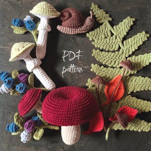 May include: A collection of crocheted items including a large red mushroom, two smaller light-colored mushrooms, a brown snail, blue and purple berries, a large green fern leaf, and small orange and red leaves. The text PDF pattern is visible.