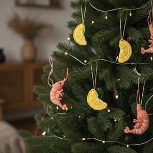 May include: A Christmas tree decorated with handmade ornaments. The ornaments include crocheted shrimp in shades of pink and yellow lemon slices. The tree is lit with small white lights, creating a festive holiday display.