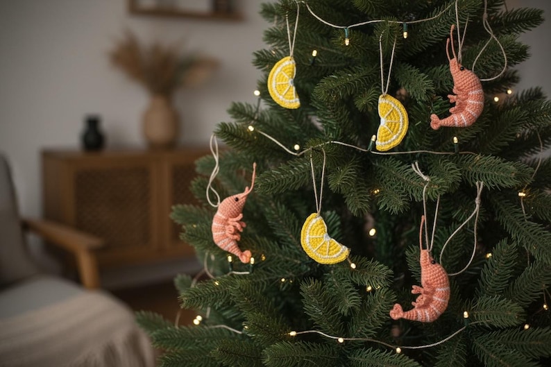 May include: A Christmas tree decorated with handmade ornaments. The ornaments include crocheted shrimp in shades of pink and yellow lemon slices. The tree is lit with small white lights, creating a festive holiday display.
