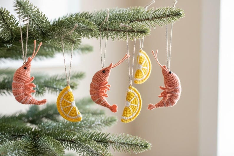 May include: Crocheted Christmas tree ornaments in the shape of shrimp and lemon slices. The shrimp are coral-colored, and the lemon slices are yellow with white details. The ornaments hang from a green Christmas tree.