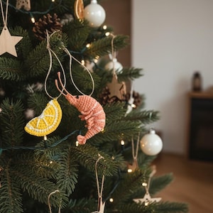 May include: A decorated Christmas tree with various ornaments. The tree features a dried orange slice, wooden star, white ball ornaments, and crocheted shrimp and lemon slice ornaments. The tree is lit with small white lights.