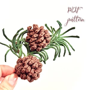 May include: Close-up of two brown crocheted pinecones with green crocheted needles. The pinecones are detailed and textured, with the text "PDF pattern" in the upper right corner.