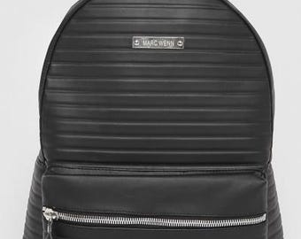 Pode incluir: Mochila preta com design canelado, alça superior e bolso frontal com zíper. A mochila apresenta um zíper prateado e um pequeno logotipo retangular que diz "MARC WENN".