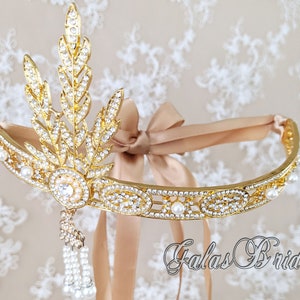 May include: A gold headband with a delicate leaf design and pearl accents. The headband is adorned with sparkling rhinestones and features a dangling pearl tassel. The headband is tied with a beige satin ribbon.