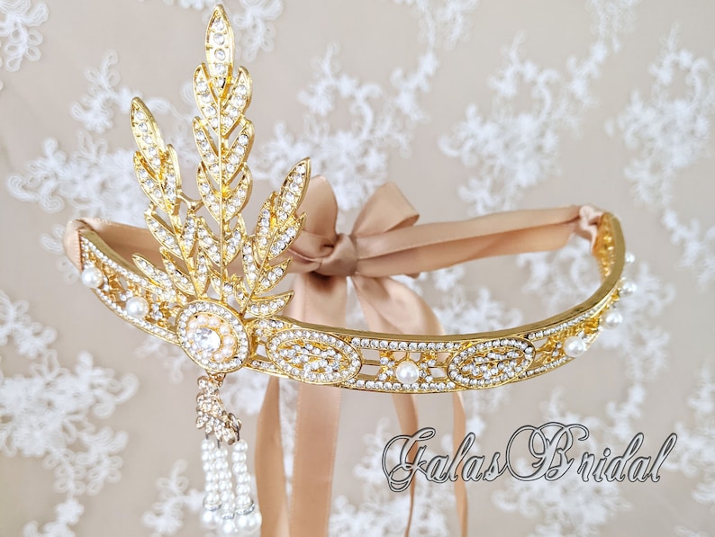May include: A gold headband with a delicate leaf design and pearl accents. The headband is adorned with sparkling rhinestones and features a dangling pearl tassel. The headband is tied with a beige satin ribbon.