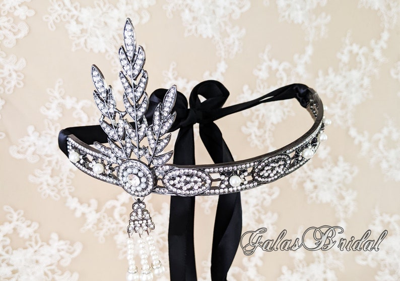 May include: A silver and black headband with a pearl and crystal design. The headband has a black ribbon tie and a dangling pearl and crystal tassel.