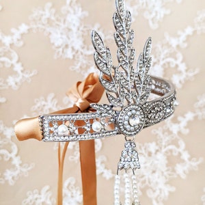 May include: A silver headband with a delicate floral design and pearl accents. The headband is adorned with rhinestones and has a dangling pearl and rhinestone drop.