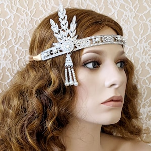 May include: A silver headband with a pearl and crystal design. The headband features a leaf-shaped design with a large crystal in the center. The headband is adorned with small pearls and crystals.