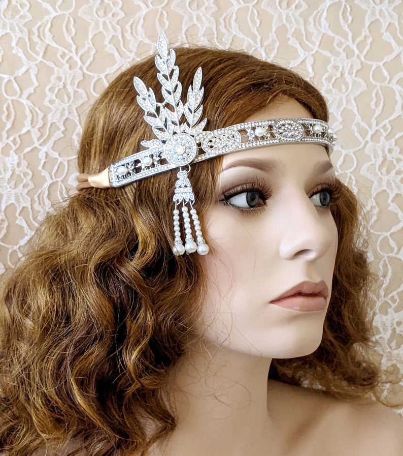 May include: A silver headband with a pearl and crystal design. The headband features a leaf-shaped design with a large crystal in the center. The headband is adorned with small pearls and crystals.
